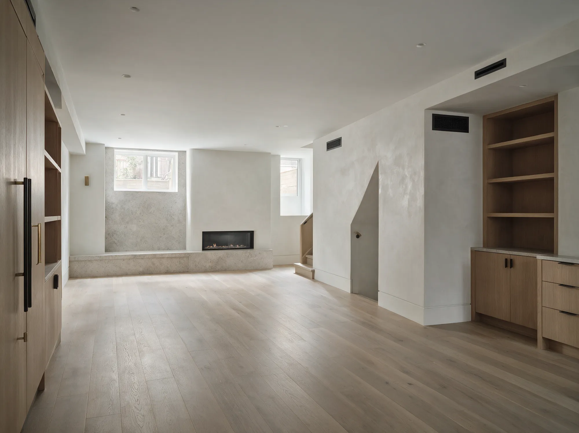 A finished basement with full-height ceilings, oak floors, a linear gas fireplace and built-in oak shelving