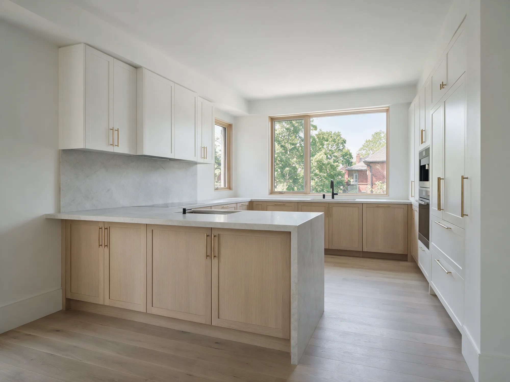 A finished kitchen renovation with white oak cabinetry, a stone-wrapped peninsula, marble backsplash and brass hardware
